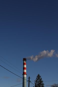 Red and white industrial chimney with smoke against blue sky background.