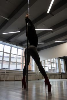 Anonymous seductive female touching metal pole with buttocks while rehearsing erotic dance in studio