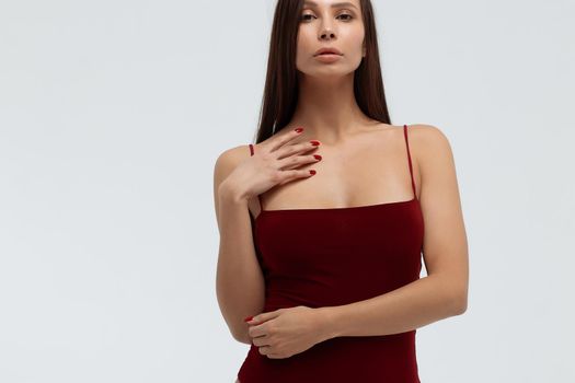 Sexy young female wearing red bodysuit and high heeled shoes standing on white background in studio and looking at camera