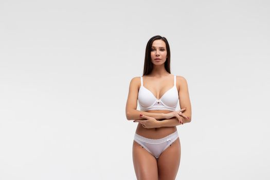 Confident female wearing white underwear standing with hands on waist on white background and looking at camera