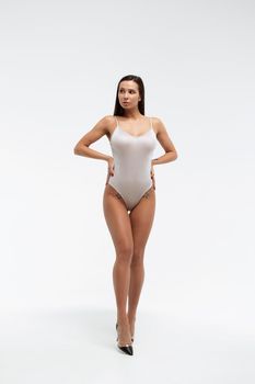 Tender female wearing bodysuit standing with folded arms on white background in studio and looking away