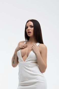 Young stylish seductive female in trendy white dress with low neckline looking erotically at camera