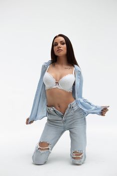 Young seductive female model in bra and shirt with denim wear standing with raised arms while looking at camera