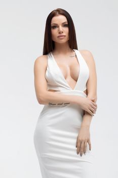 Young stylish seductive female in trendy white dress with low neckline looking erotically at camera