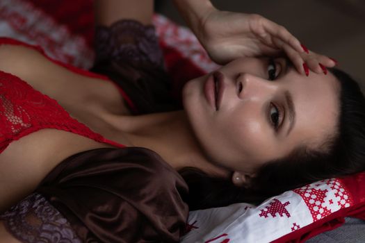 Side view of sexual young female with long dark hair in elegant red bra lying on comfortable bed with closed eyes near decorated Christmas tree