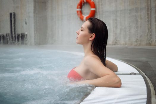 Seductive woman in pink bra crossing arms and looking away while resting in clean water of hot spring on resort