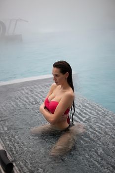 Sexy barefoot female in red swimsuit lying on grates in water of hot spring on resort