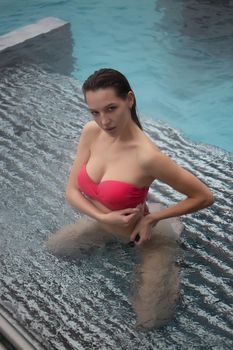 Sexy barefoot female in red swimsuit lying on grates in water of hot spring on resort