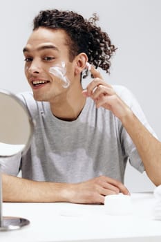 handsome guy in a white T-shirt in front of a mirror skin care Lifestyle. High quality photo