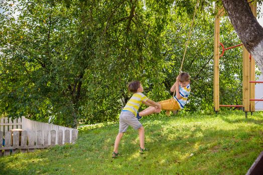 Two adorable happy little boys is having fun on a rope swing which he has found while having rest outside city. Active leisure time with children.