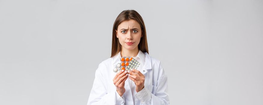 Pharmacy, healthcare workers, insurance and hospitals concept. Concerned and skeptical female doctor in white scrubs, look suspicious, dont like this medicine, smirk disappointed, show bad medicine.