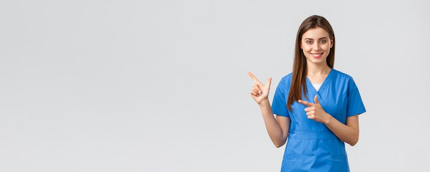 Healthcare workers, prevent virus, insurance and medicine concept. Professional smiling, attractive female nurse or doctor in blue scrubs, physician pointing finger left at banner, recommend clinic.