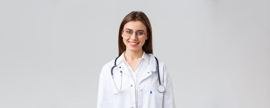 Healthcare workers, medicine, insurance and covid-19 pandemic concept. Smiling attractive female doctor, physician in white scrubs with stethoscope and glasses look upbeat at camera.