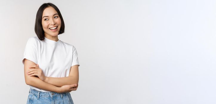 Portrait of happy asian woman smiling, posing confident, cross arms on chest, standing against studio background.