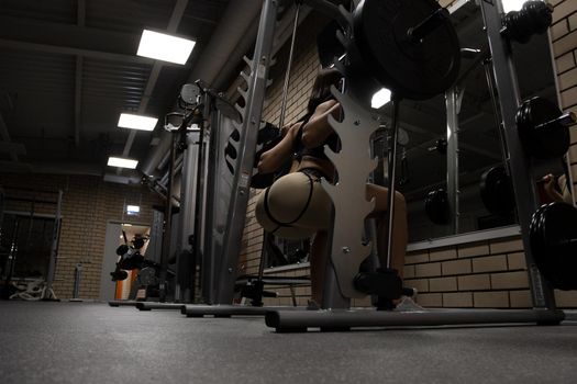 Low angle back view of slim athletic woman in sportswear with perfect sexy buttocks doing squats with heavy barbell during workout in gym