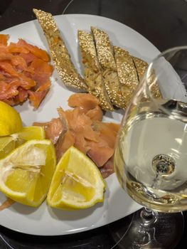 Romantic still life with a glass of white wine on the table, a plate with salted and smoked red fish, slices of lemon and bread. High quality photo