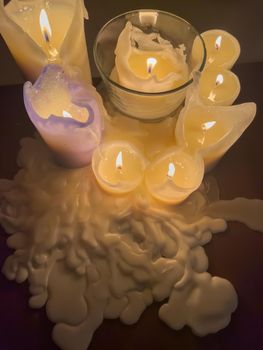 several burning candles stand on a table in a dark interior, molten wax around the candles, high angle view. High quality photo