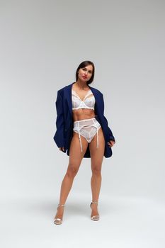 Confident female wearing white underwear standing with hands on waist on white background and looking at camera