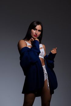 Back view alluring gorgeous brunette wearing white lace lingerie lowering jacket and looking at camera over shoulder during photo session in studio