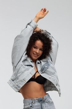 Full body of confident young barefoot female model with curly hairstyle wearing trendy denim jacket and jeans