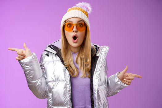 Lifestyle. Impressed blond girl gasping widen eyes surprised folding lips wow sound check out incredible discounts winter equipment pointing left right cannot choose standing astonished purple background.