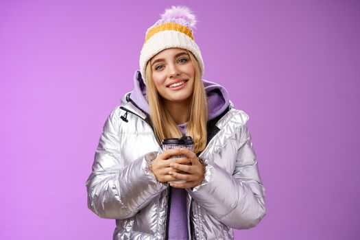 Tender relaxed cheerful smiling blond girl look pleased relieved drinking hot coffee cacao enjoying nice heartwarming moment look camera delighted gentle grin, wearing winter jacket hat.