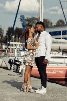 Side view of cheerful couple in love hugging in harbor with boats on sunny day in summer