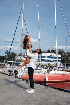 Side view of cheerful couple in love hugging in harbor with boats on sunny day in summer