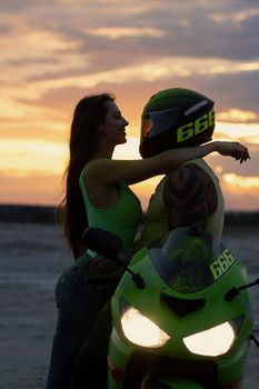 Side view of couple in love tenderly hugging near motorcycle parked on sandy seashore against sundown sky