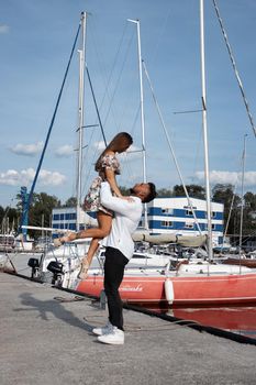 Side view of cheerful couple in love hugging in harbor with boats on sunny day in summer