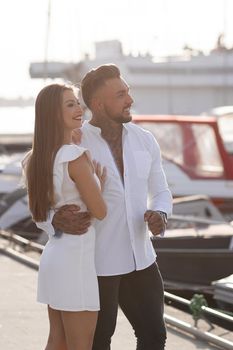 Loving couple hugging while standing on embankment near boats on sunny day in summer