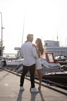 Loving couple hugging while standing on embankment near boats on sunny day in summer