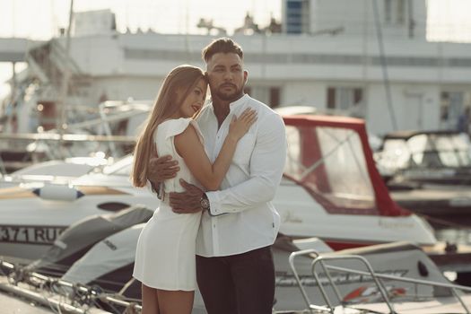 Loving couple hugging while standing on embankment near boats on sunny day in summer