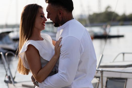 Loving couple hugging while standing on embankment near boats on sunny day in summer