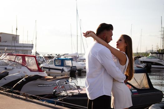 Loving couple hugging while standing on embankment near boats on sunny day in summer