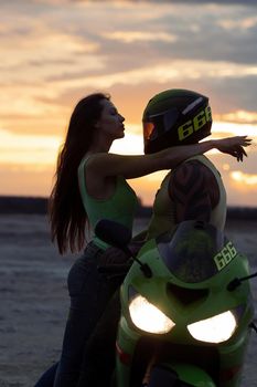 Side view of couple in love tenderly hugging near motorcycle parked on sandy seashore against sundown sky