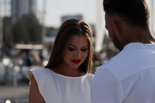 Loving couple in trendy outfits embracing while standing in port with boats in summer