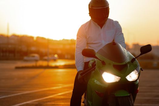 Unrecognizable stylish male motorcyclist in helmet sitting on parked motorbike in city on background of sunset sky