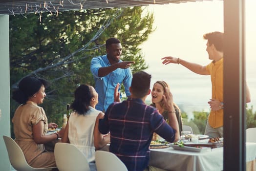 Shot of a group of friends enjoying a meal and drinks together around a table at a gathering outdoors.