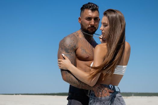 Seductive female in swimsuit and fit male with naked torso hugging while standing on sandy seashore on sunny day in summer