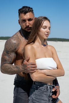 Seductive female in swimsuit and fit male with naked torso hugging while standing on sandy seashore on sunny day in summer