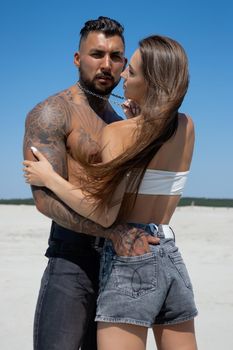 Seductive female in swimsuit and fit male with naked torso hugging while standing on sandy seashore on sunny day in summer