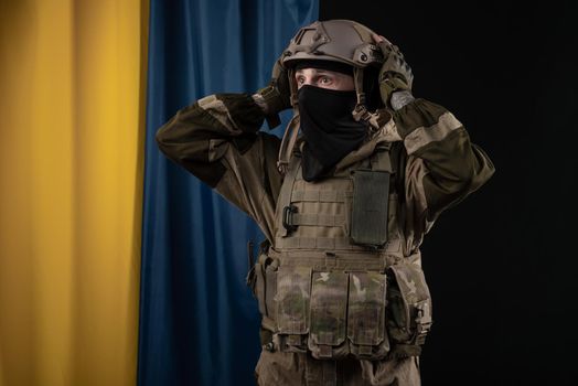 male soldier in a military uniform and helmet with a weapon on the background of the national flag of Ukraine grabbed his head