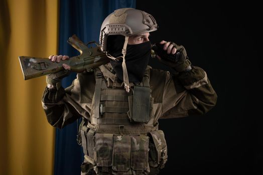 male soldier in a military uniform and helmet with a weapon on the background of the national flag of Ukraine