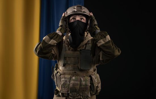 male soldier in a military uniform and helmet on the background of the national flag of Ukraine