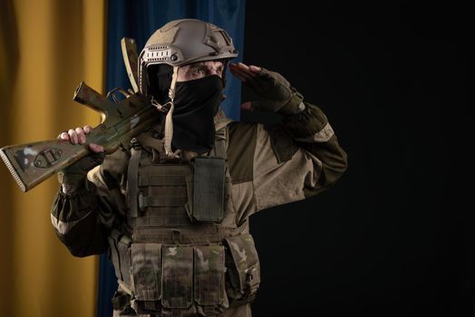 male soldier in a military uniform and helmet with a weapon on the background of the national flag of Ukraine