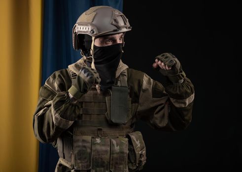 male soldier in a military uniform and helmet on the background of the national flag of Ukraine