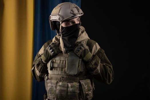 male soldier in a military uniform and helmet on the background of the national flag of Ukraine