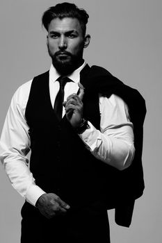 Bearded Hispanic guy in dark vest and white shirt with tie looking at camera with hands in pockets in studio