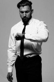 Bearded Hispanic guy in dark vest and white shirt with tie looking at camera with hands in pockets in studio